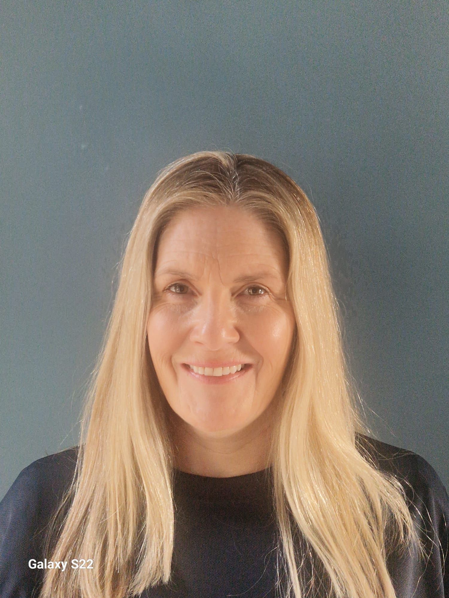 Smiling blonde woman in a dark top against a plain gray background