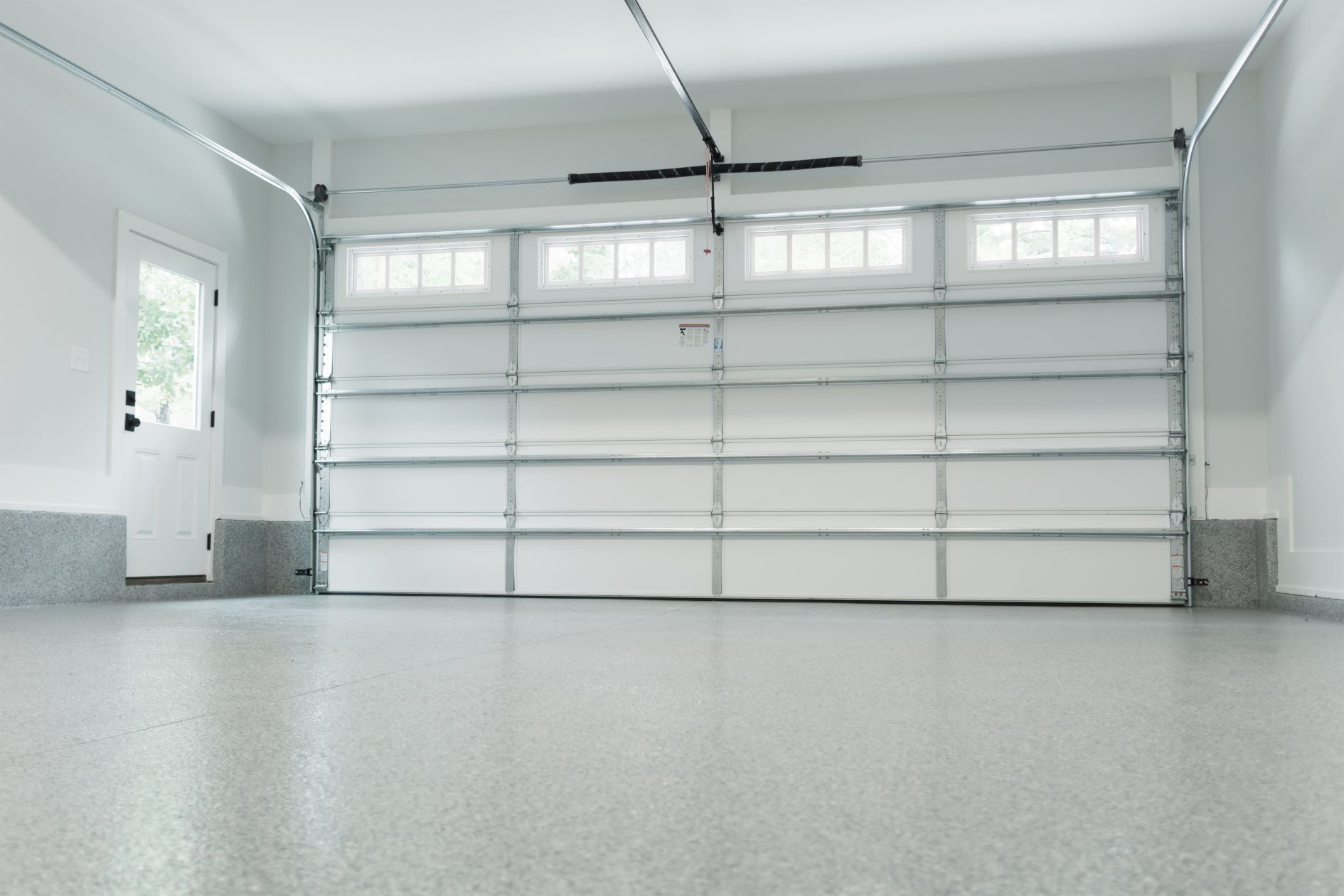 An empty garage with a white garage door and a gray floor.