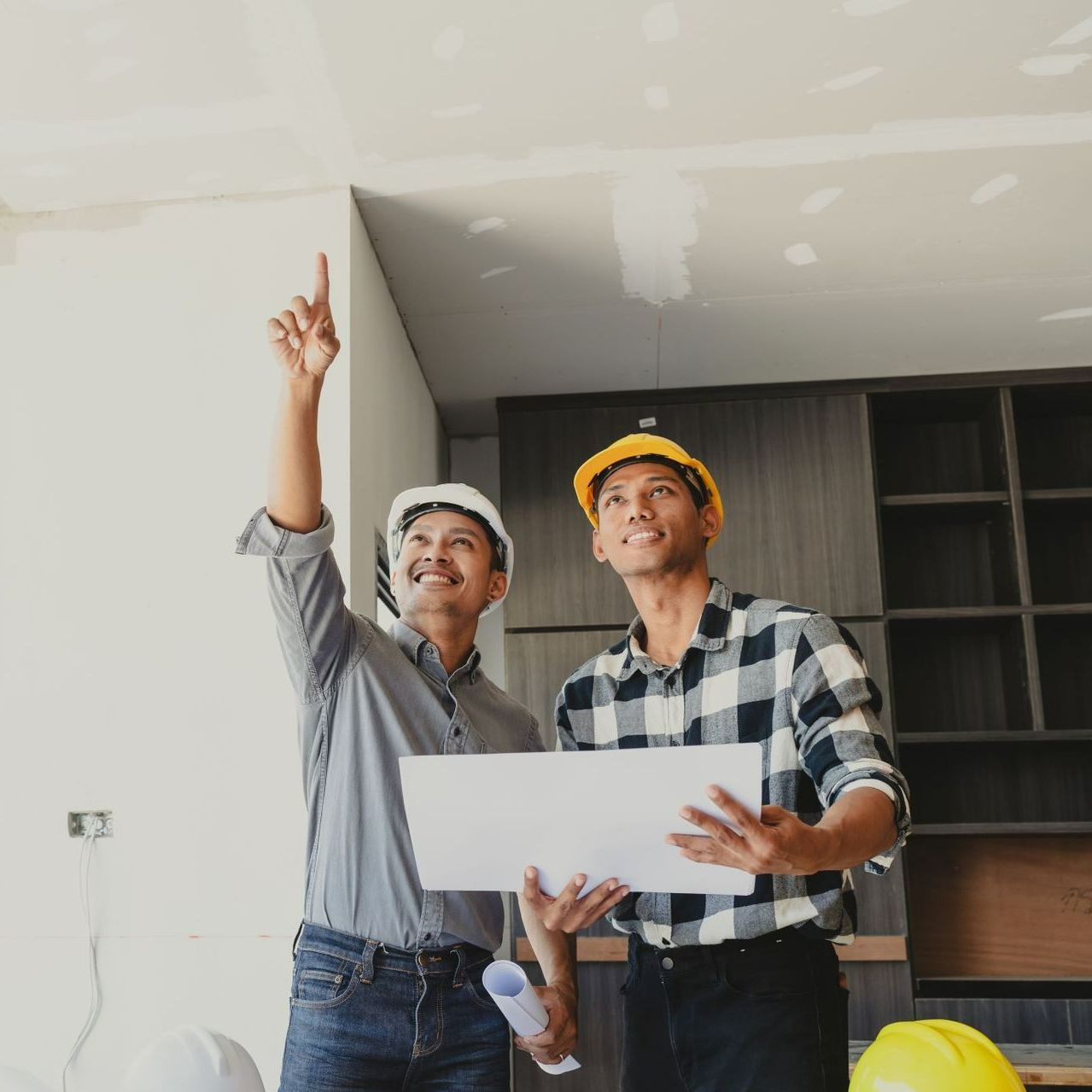 Two men wearing hard hats are looking up at the ceiling.