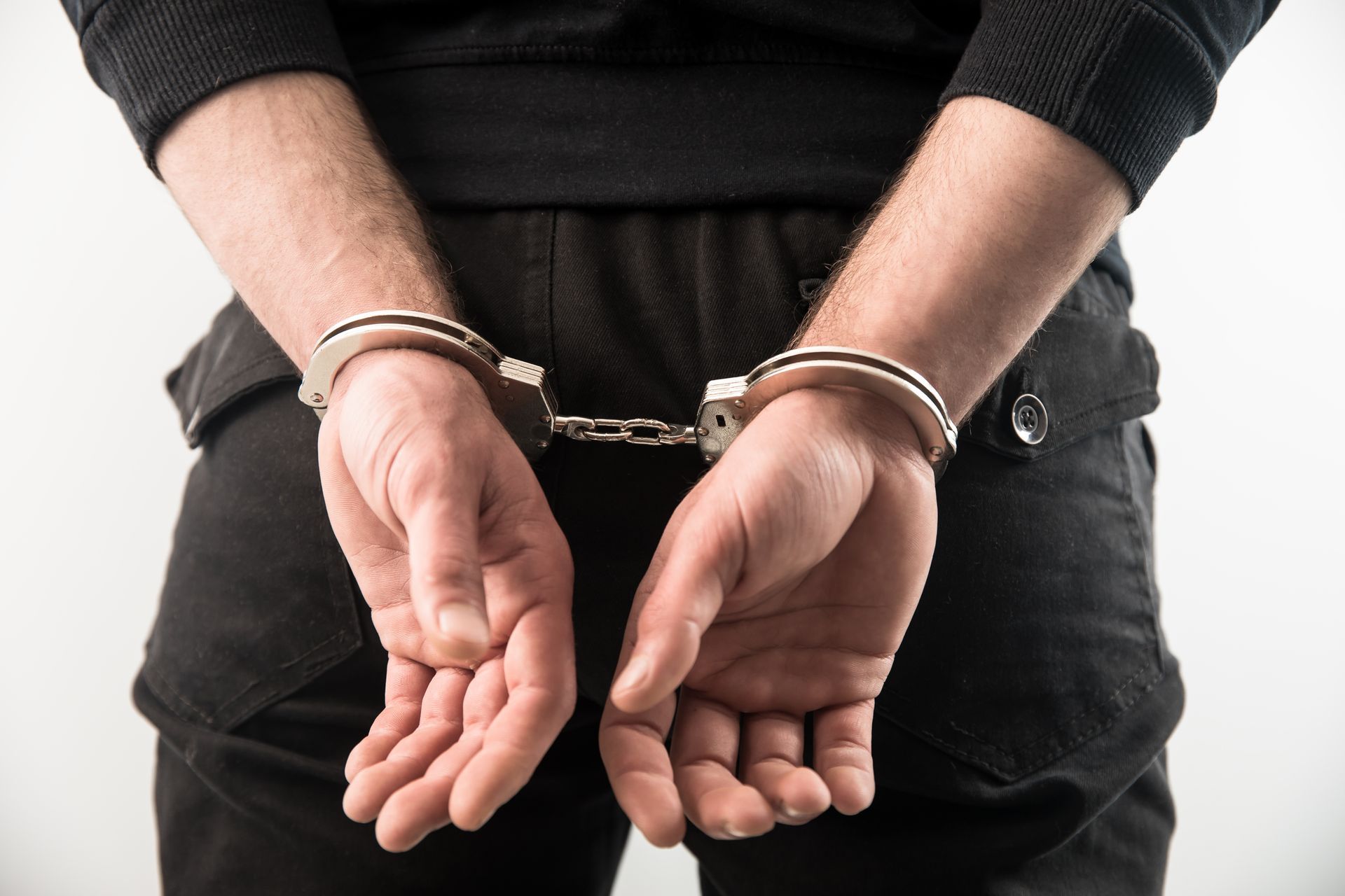 Person in black pants and top with hands cuffed behind their back.