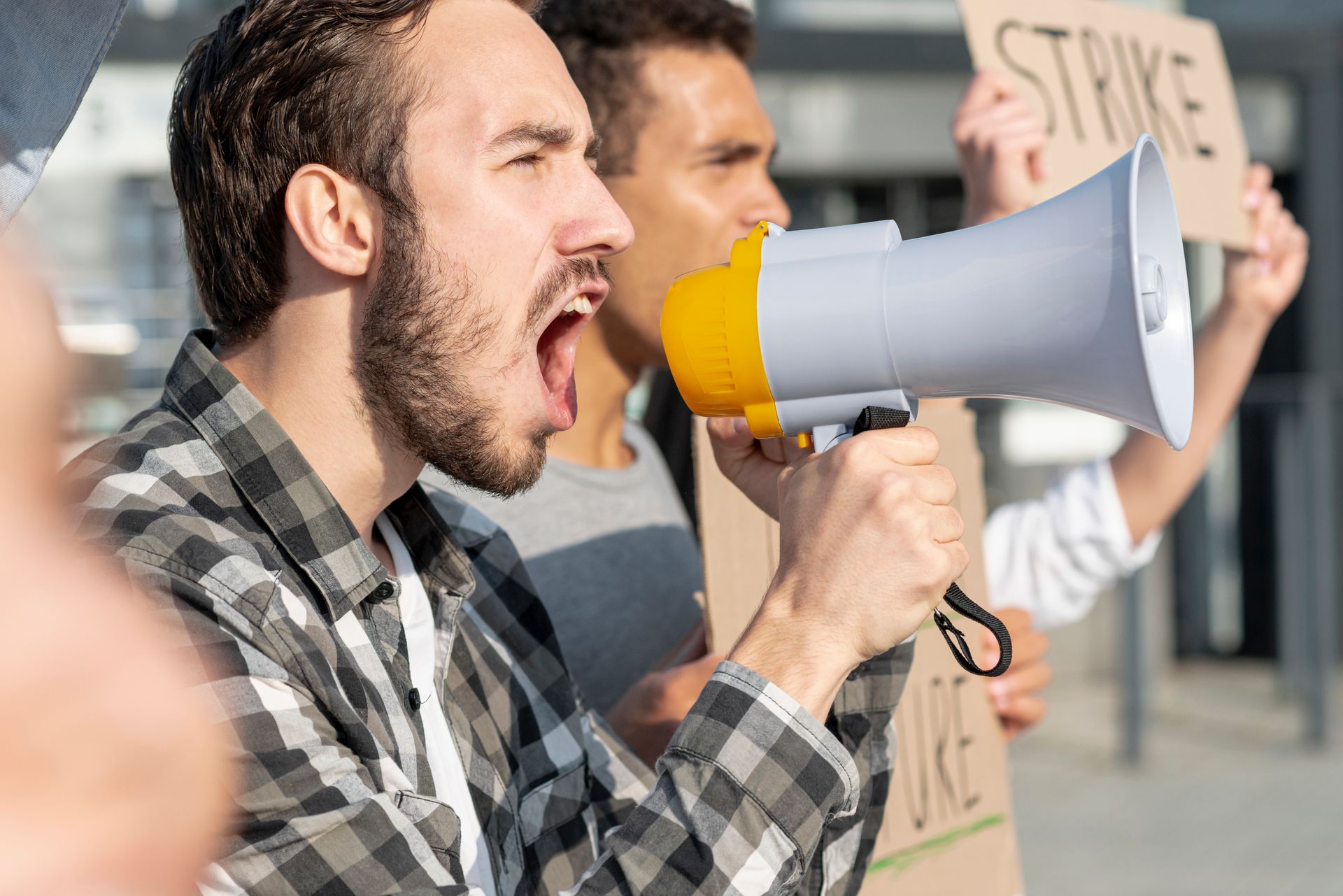 Man with megaphone shouts at a protest; another holds