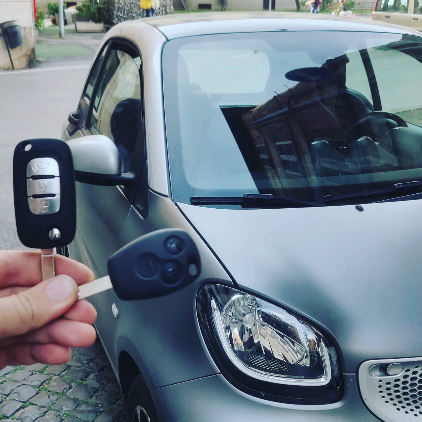 Una mano che impugna il telecomando di un'auto si trova vicino allo specchietto laterale e alla maniglia della portiera di un'auto argentata.