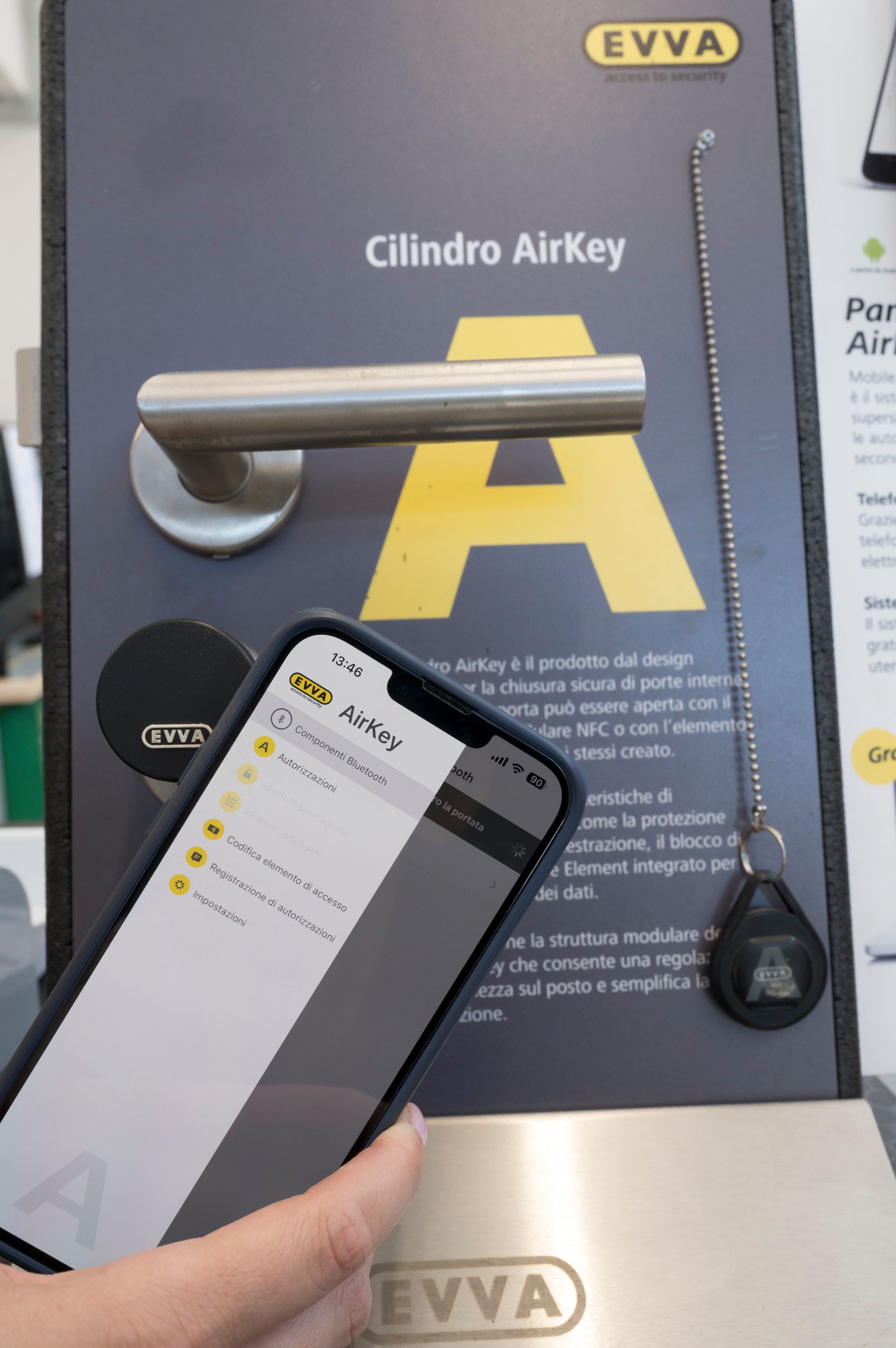 Una mano che tiene in mano un telefono sta scansionando il display di una serratura EVVA AirKey con un grande logo A giallo.