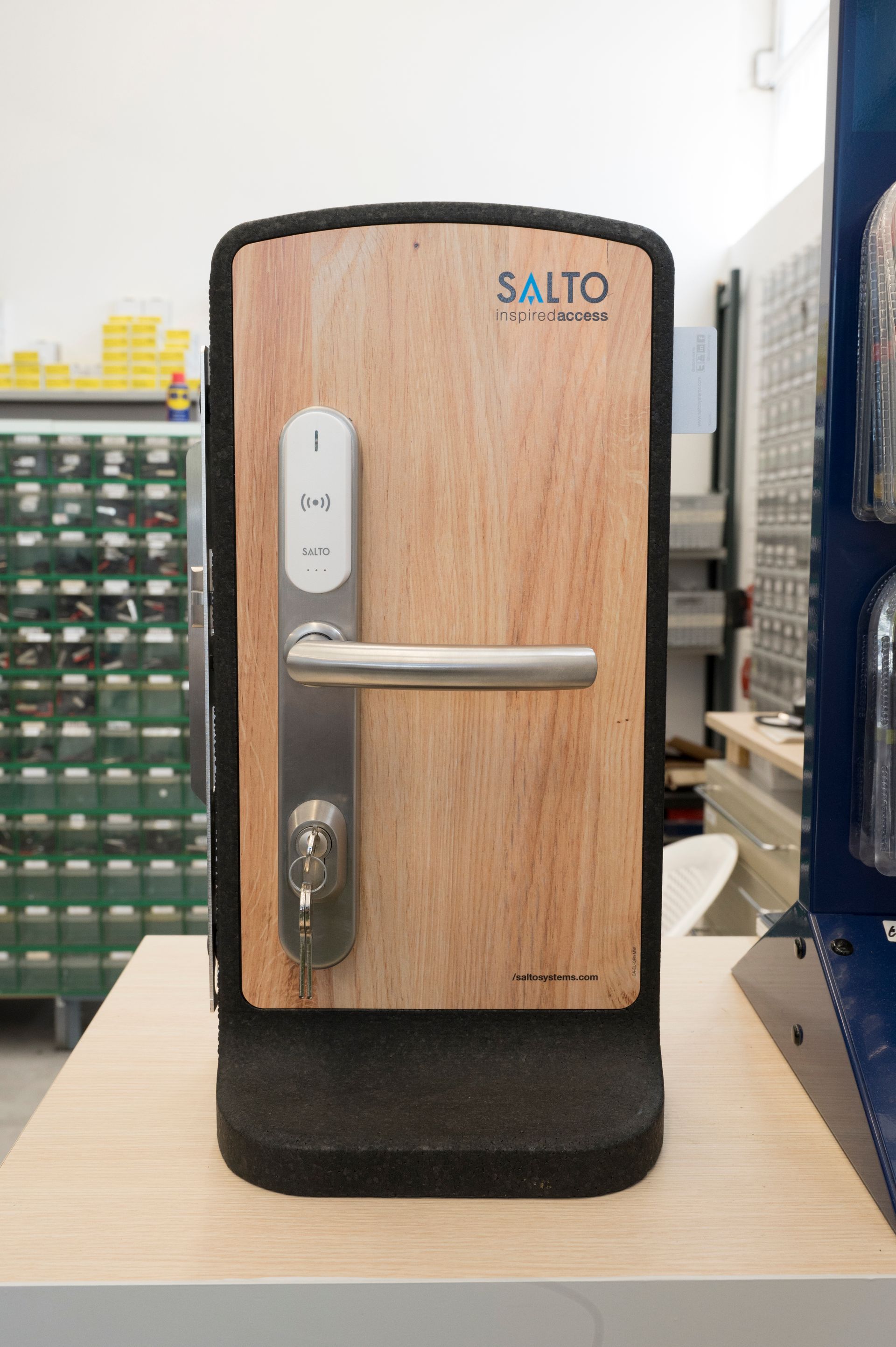 Vetrina per serratura elettronica con finitura effetto legno, posizionata su un bancone, con maniglia argentata e base nera.