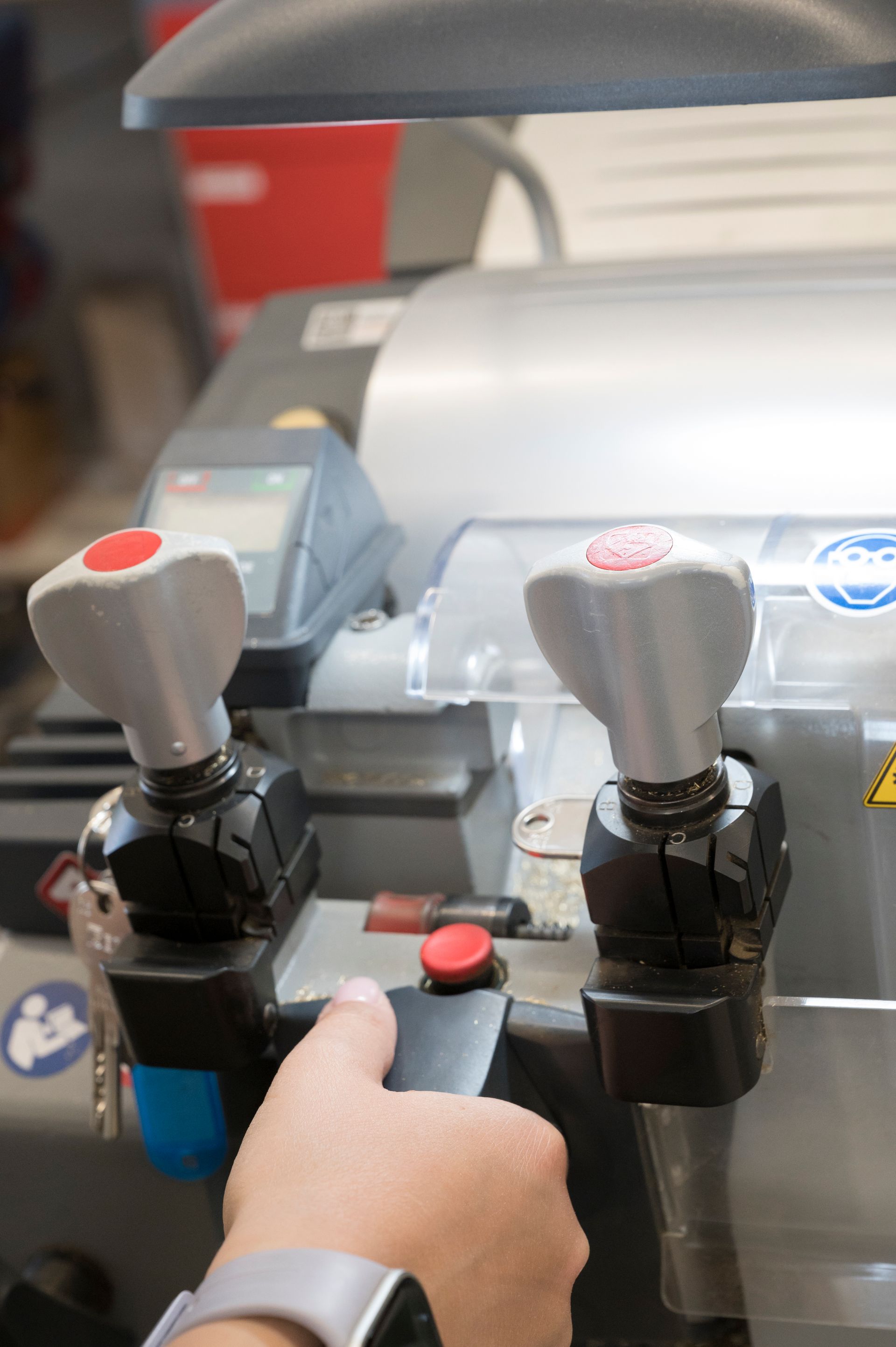Una mano preme un pulsante rosso accanto a due joystick grigi sul pannello di controllo di una macchina.