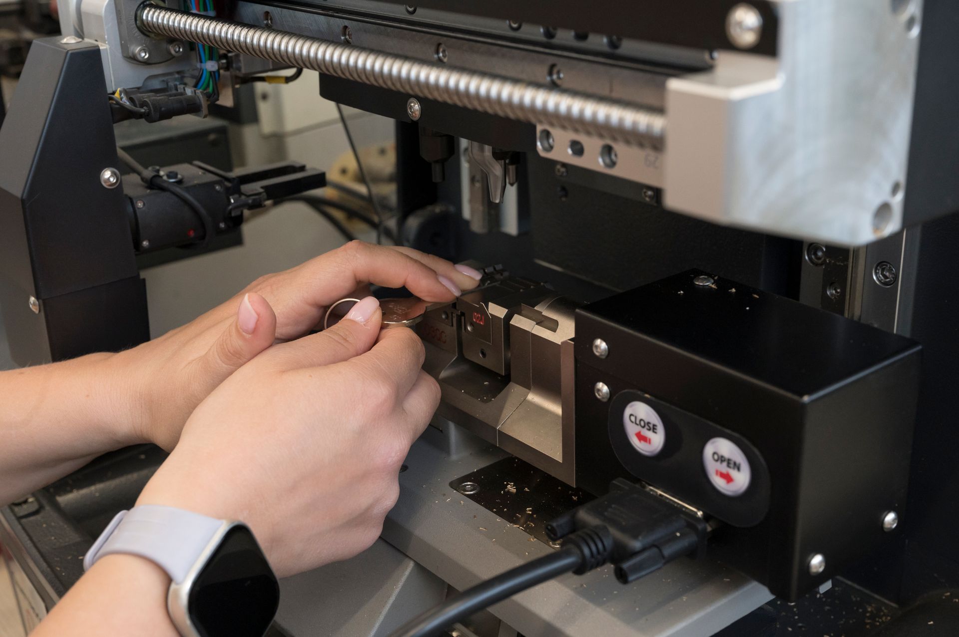 Mani che regolano un piccolo componente di una macchina all'interno di un dispositivo industriale nero e argento.