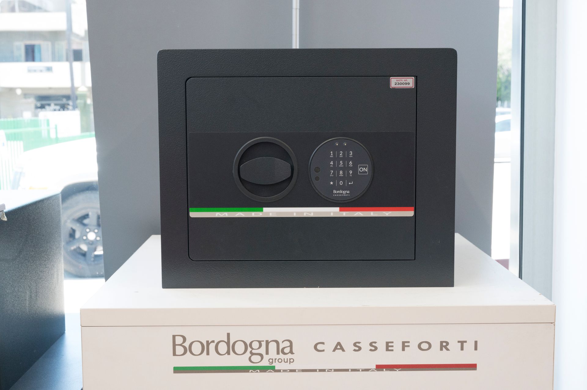 Cassaforte nera Bordogna Casseforti esposta su un supporto in vetrina, con strisce verdi e rosse.