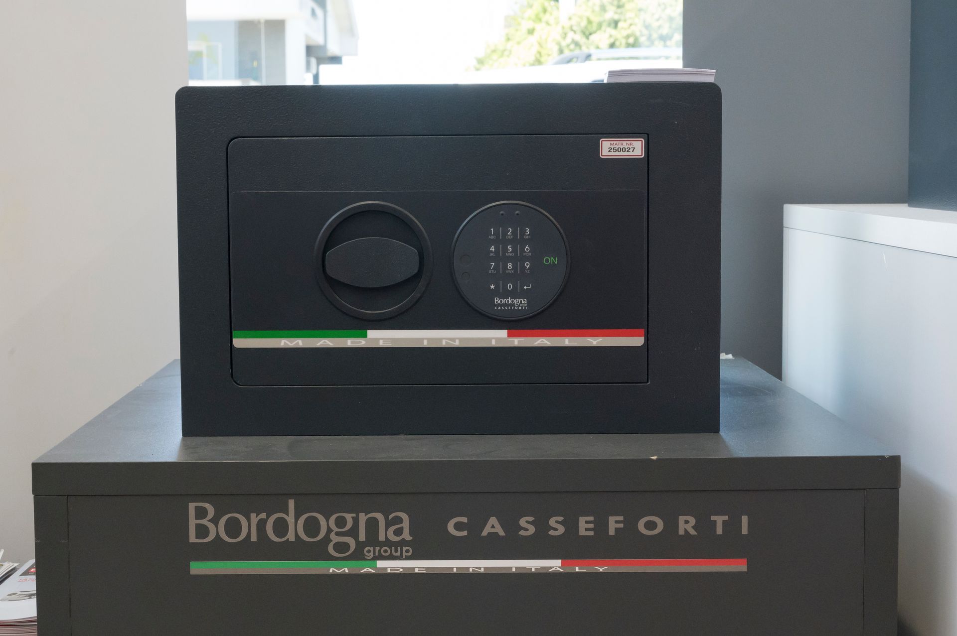 Cassaforte Casseforti Bordogna nera con tastiera, posizionata su un piedistallo con striscia verde e rossa.