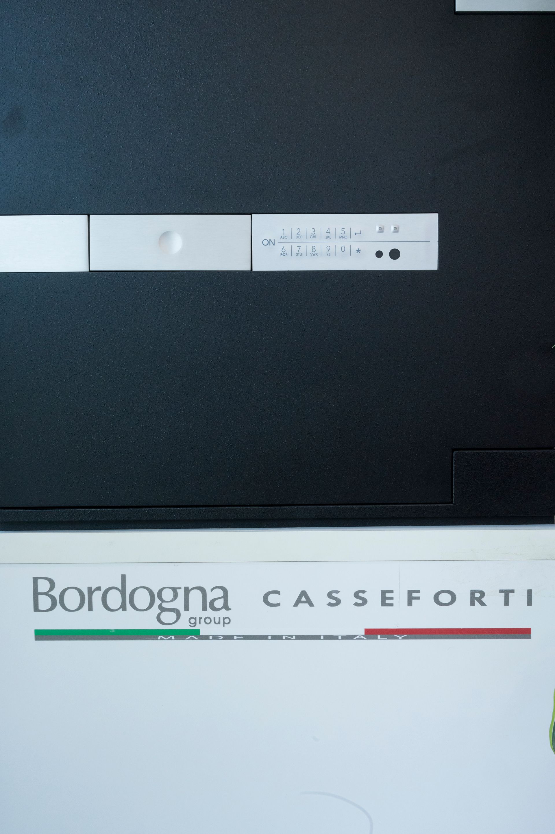 Logo Bordogna Casseforti su un pannello bianco sotto una parete scura, con una piccola barra di controllo sopra.