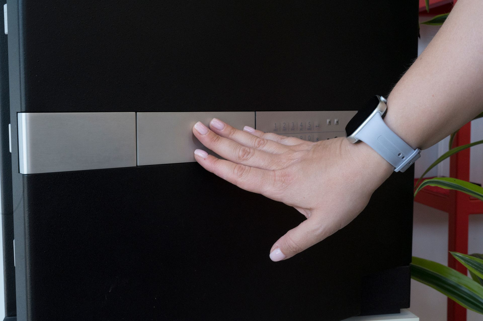 Una mano preme una striscia d'argento su un mobile nero, con un braccialetto bianco visibile.