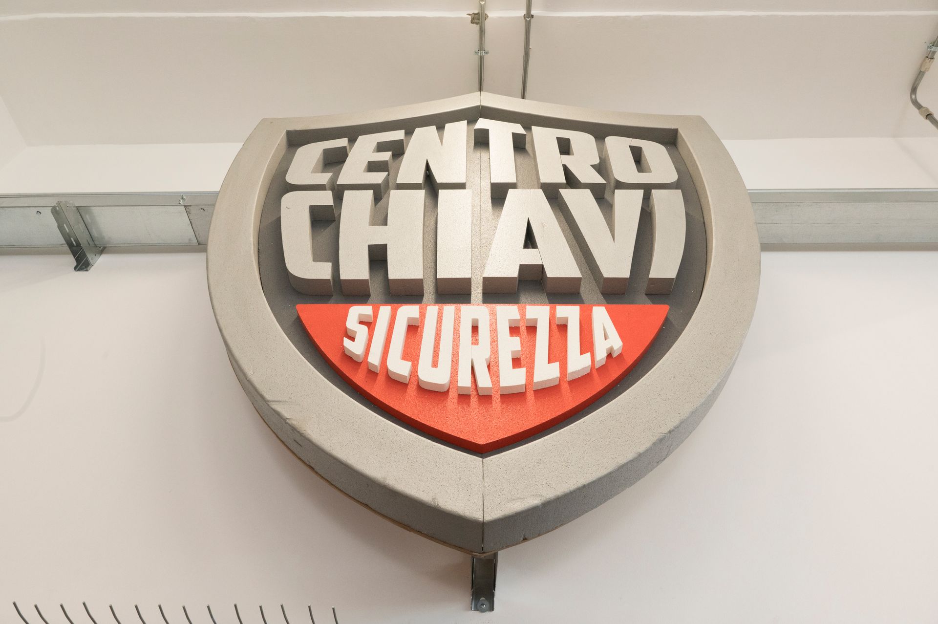 Insegna a forma di scudo del Centro Chiavi Sicurella, in nero, bianco e rosso, su un muro.