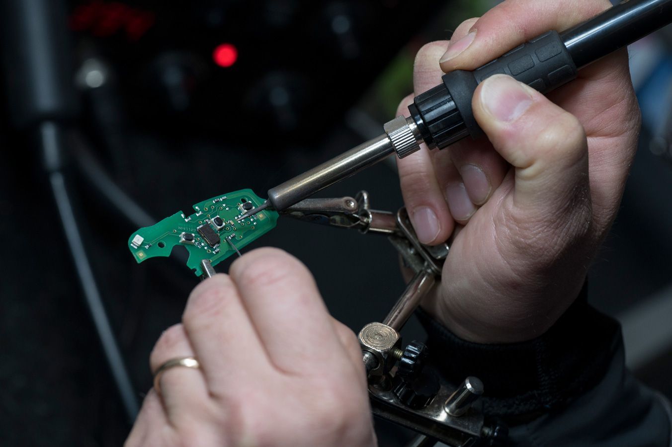 Mani che saldano un piccolo circuito stampato verde con un saldatore in un'officina