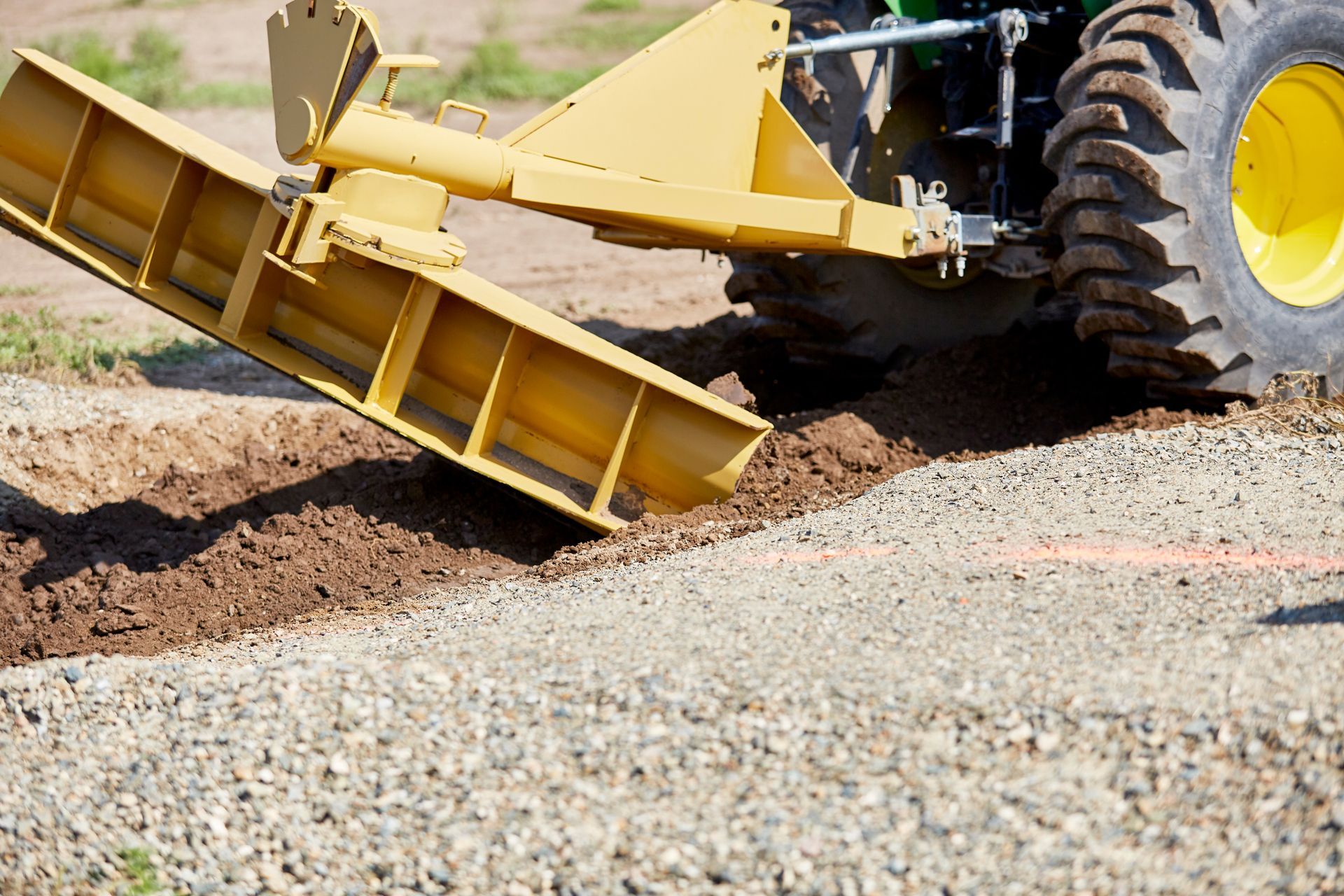 Yellow tractor grading gravel road with blade.