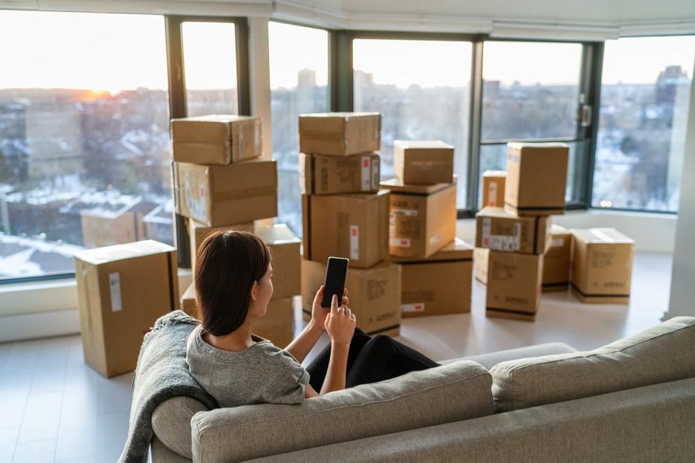 A Woman Is Sitting On A Couch In Front Of A Pile Of Cardboard Boxes — Brisbane Moving & Storage In Miles, QLD