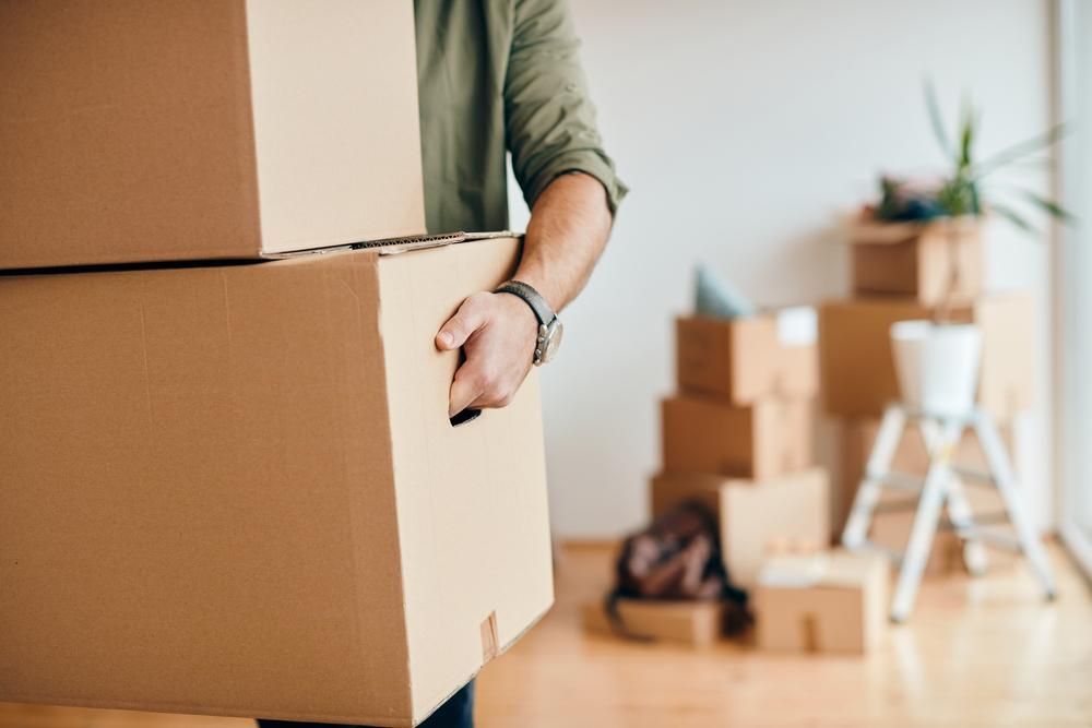 A Man Is Carrying A Stack Of Cardboard Boxes In A Room — Brisbane Moving & Storage In Miles, QLD