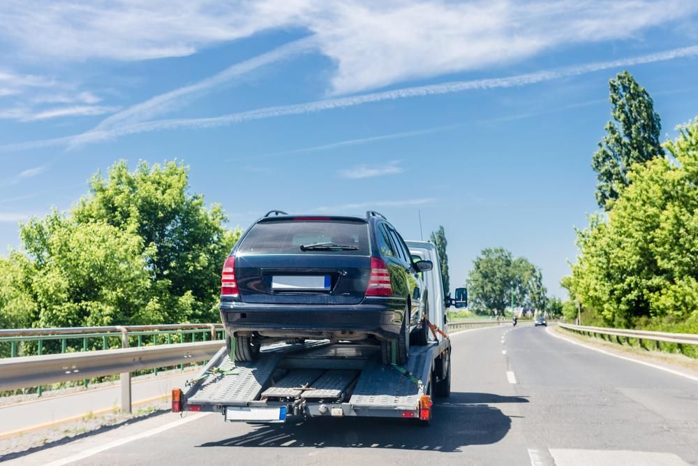 A Car Is Being Towed Down A Highway By A Tow Truck — Brisbane Moving & Storage In Acacia Ridge, QLD