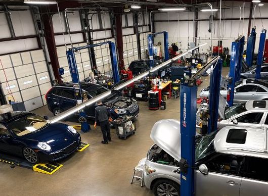 Auto repair shop with several cars on lifts and mechanics working inside a large garage