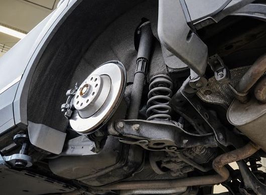 Close-up of a car’s rear wheel and suspension with the wheel removed, showing the brake rotor and coil spring.