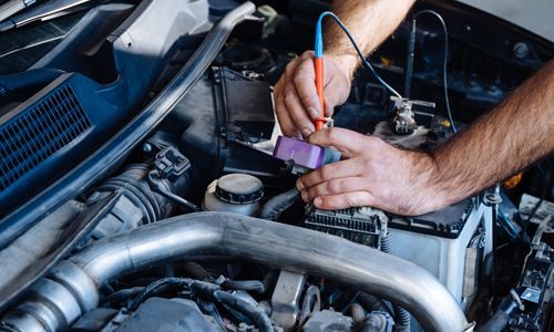 Mechanic testing a car battery with a multimeter in an engine bay
