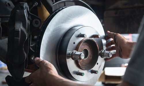 Mechanic’s hands inspecting a shiny car brake rotor in a workshop