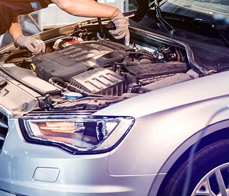 Mechanic inspecting a silver car engine with hood open in a workshop