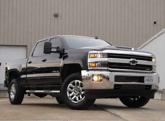Black Chevrolet pickup truck parked on wet pavement in front of a beige industrial building