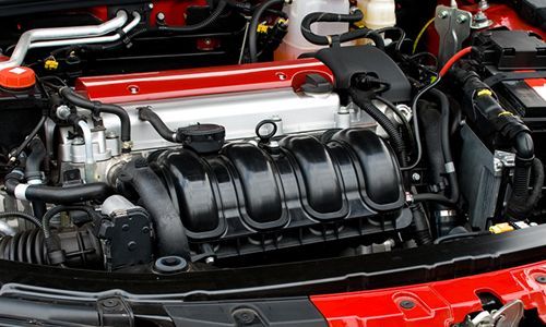 Close-up of a car engine bay with a black intake manifold and red body panels.