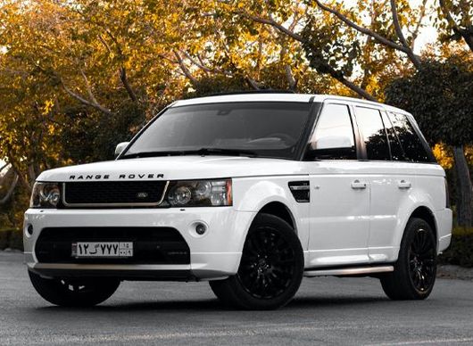 White Range Rover SUV parked on a road with autumn trees in the background