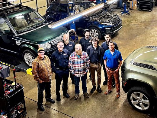 Group of people standing in an auto shop with several vehicles and a wet floor