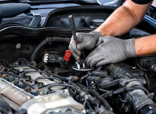 Mechanic using a wrench to repair a car engine in an open hood bay