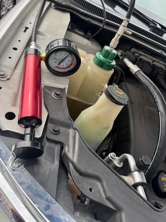 Engine bay with a pressure gauge and two translucent fluid reservoirs beside red and green components.
