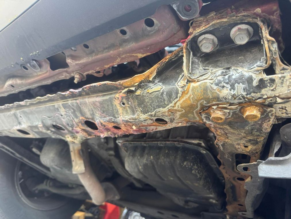 Rusty, corroded underside of a vehicle with damaged metal and exposed bolts