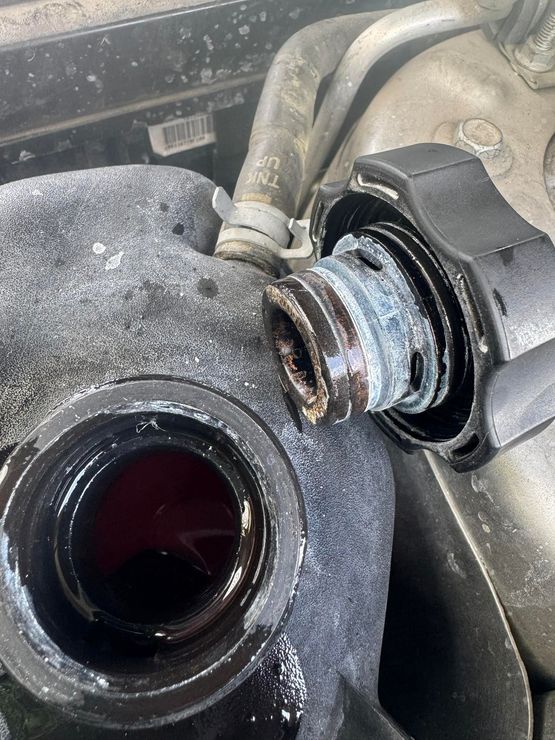 Close-up of a car engine coolant reservoir cap and filler neck with dark fluid inside