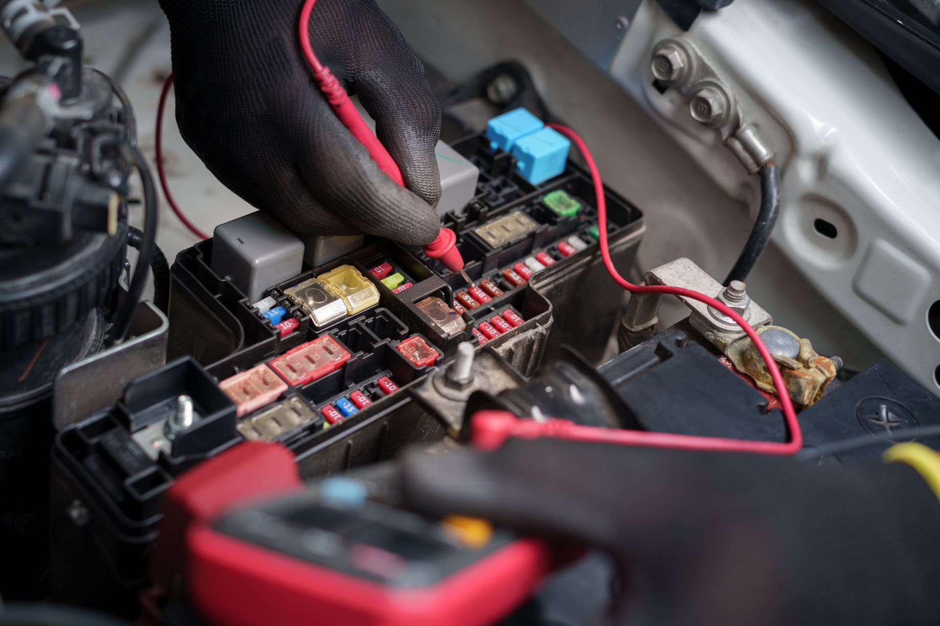 Gloved hands inspecting a car fuse box and wiring in the engine bay