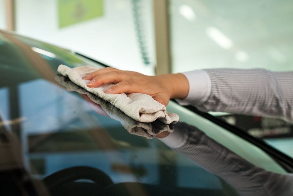 A Person is Cleaning a Car Windshield With a Towel — Keppel Coast Windscreens in Coorooman, QLD