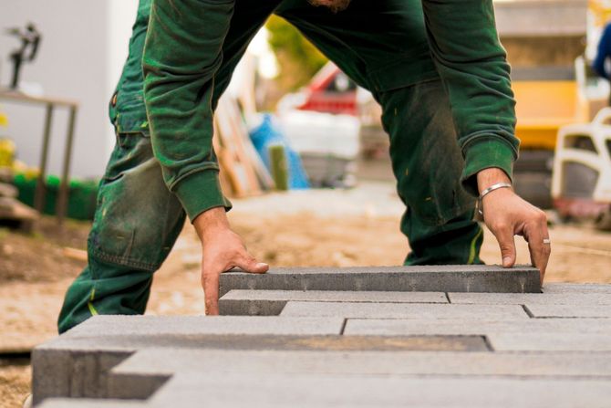 Worker in green clothes laying gray paving blocks at a construction site