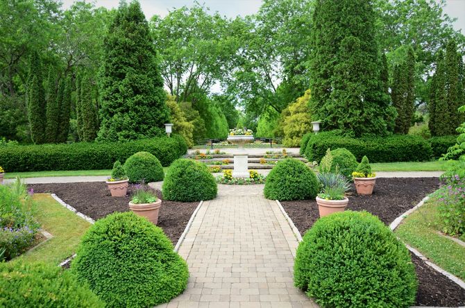 Formal garden with stone path, manicured shrubs, terraced flower beds, and a fountain in the distance