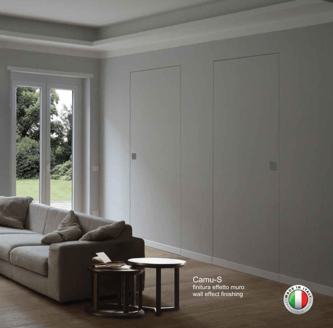 Soggiorno con pareti bianche, un divano, tavolini e due porte nascoste. Una finestra sulla sinistra.