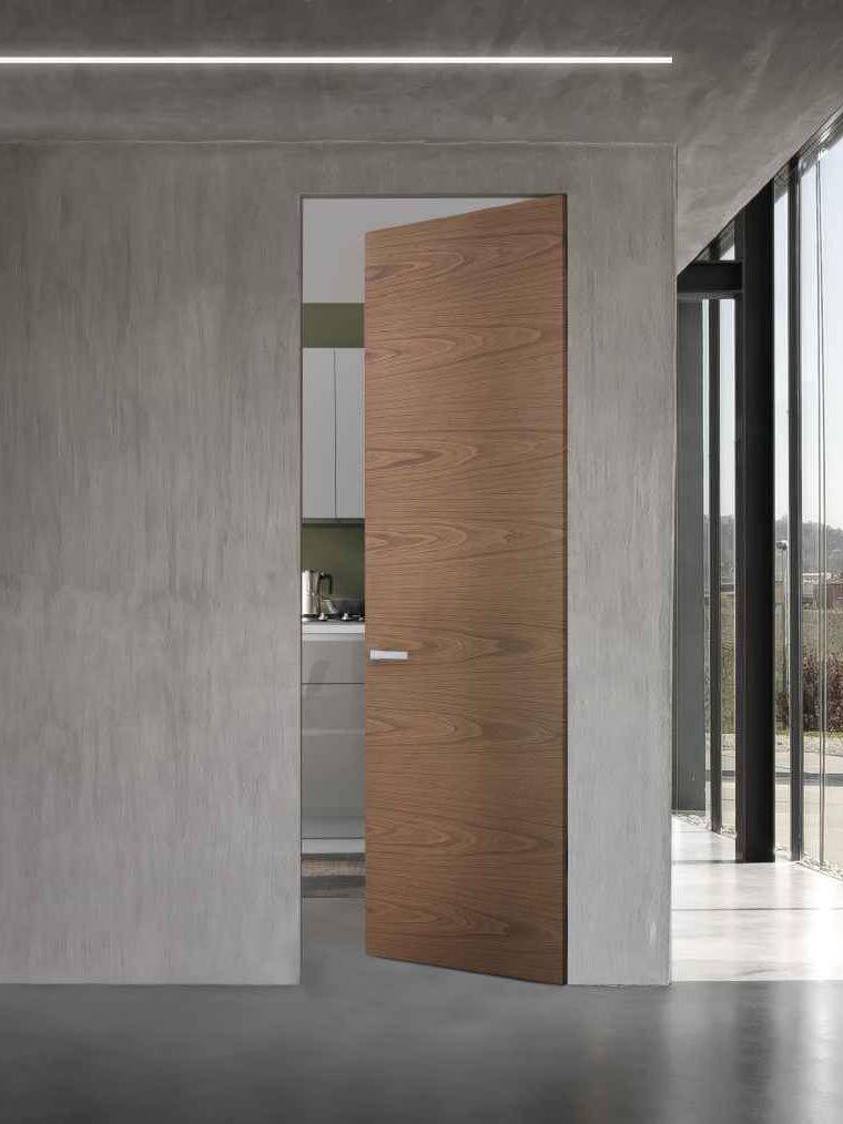 Porta in legno parzialmente aperta in una stanza moderna e minimalista; pareti in cemento, luce intensa.