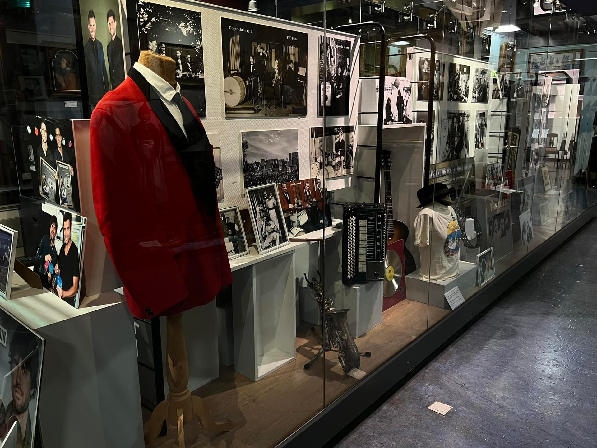 Rode blazer op een paspop in een museumvitrine met foto's en voorwerpen.