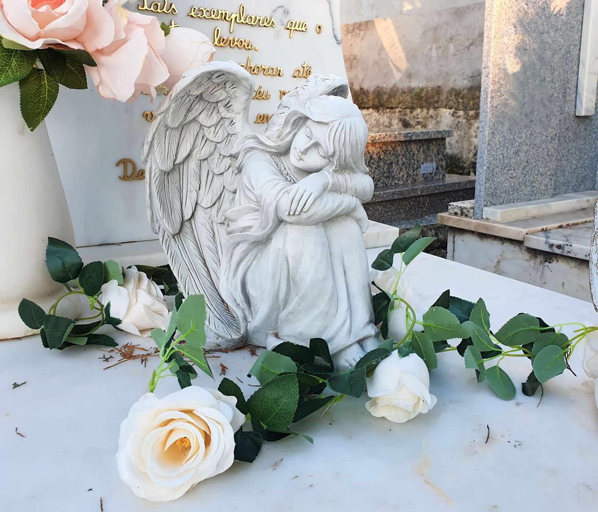 Statua di un angelo bianco su una lapide, circondata da rose bianche e rosa.