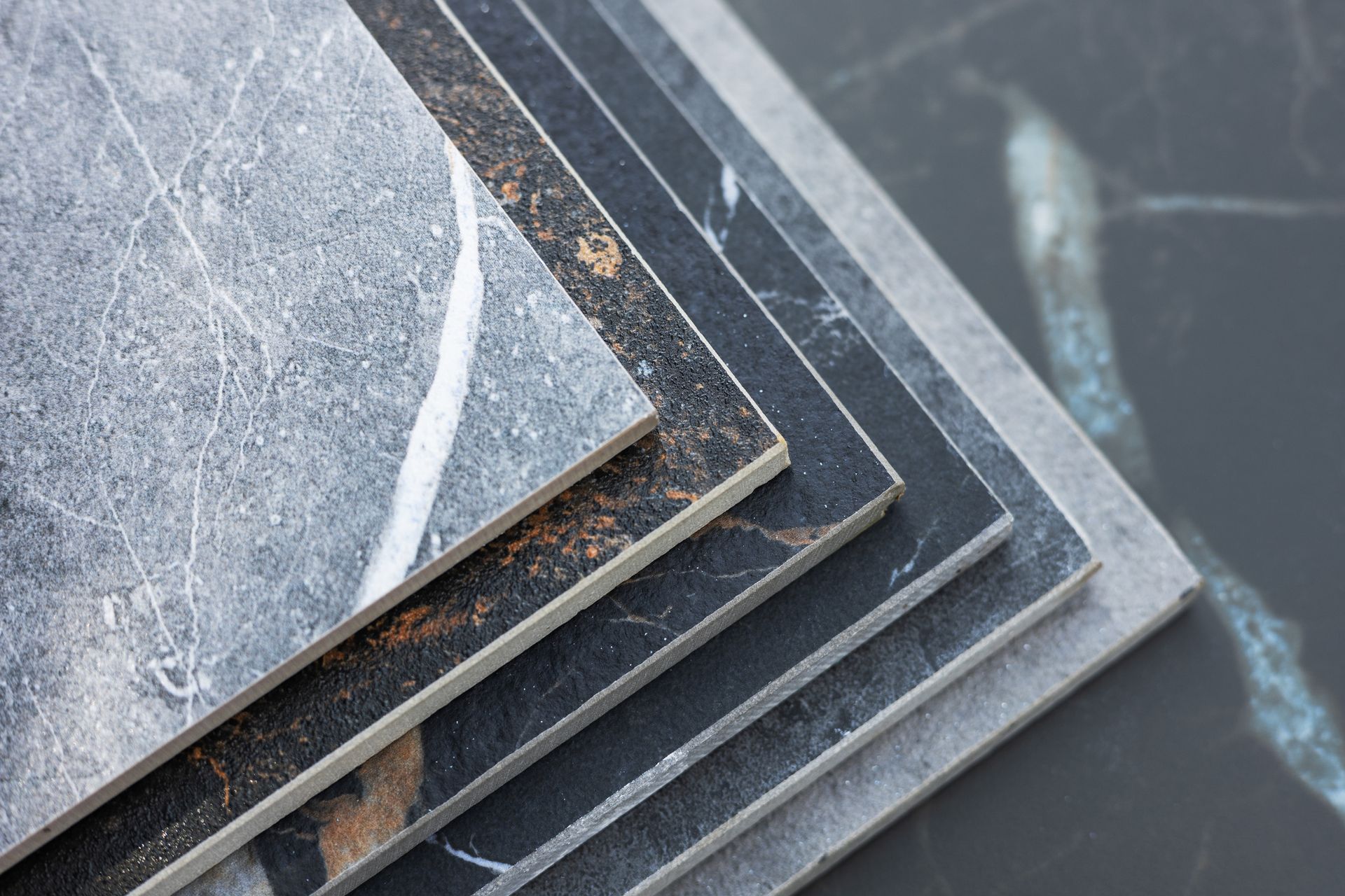 Pila di piastrelle grigie, nere e con motivi marmorei, che presentano diverse texture e design.