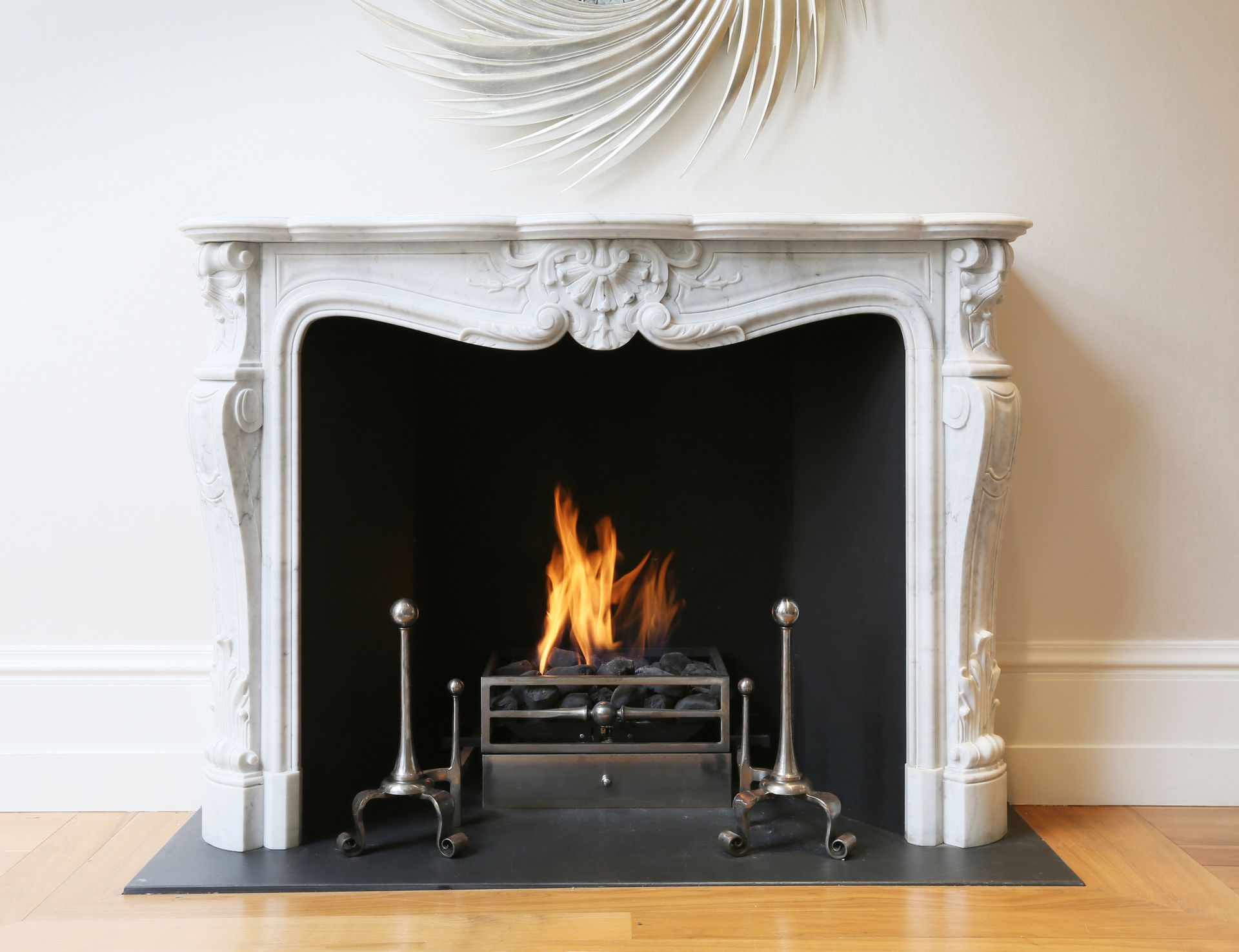 Caminetto bianco decorato con fiamme ardenti, griglia metallica e utensili.