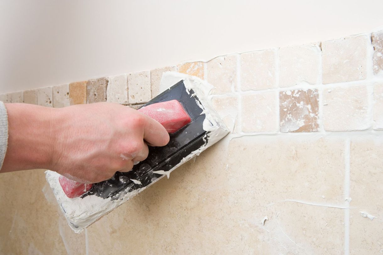 Applicazione manuale dello stucco sulle piastrelle con un frattazzo su un muro.