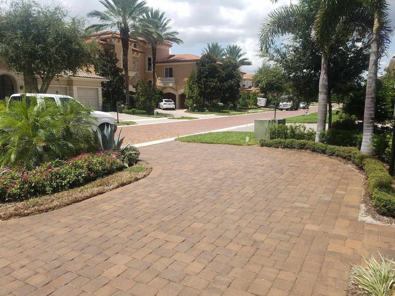 Brick driveway leading to a suburban home with palm trees and landscaped greenery
