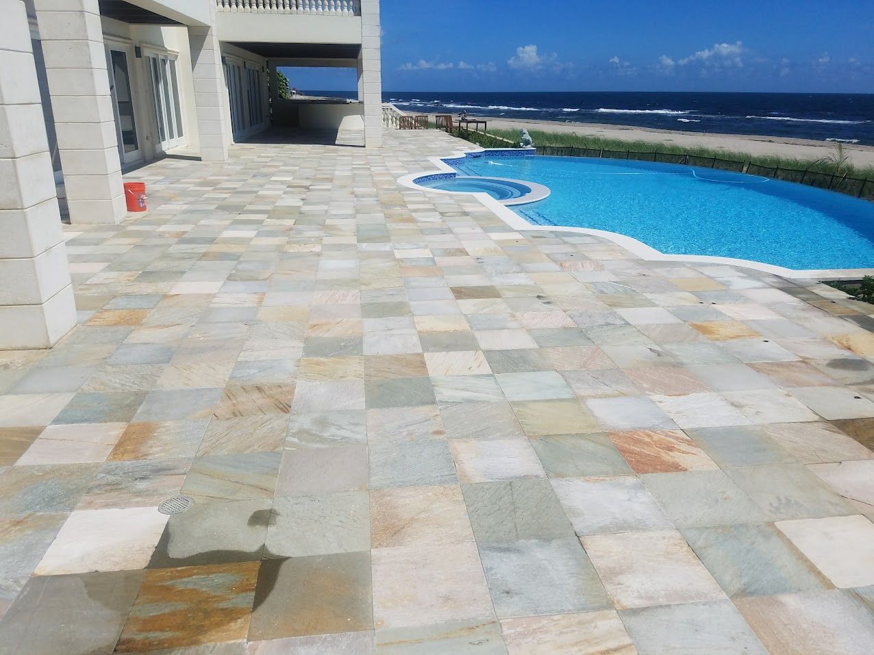 Oceanfront patio with a curved blue swimming pool beside a white building under a clear sky