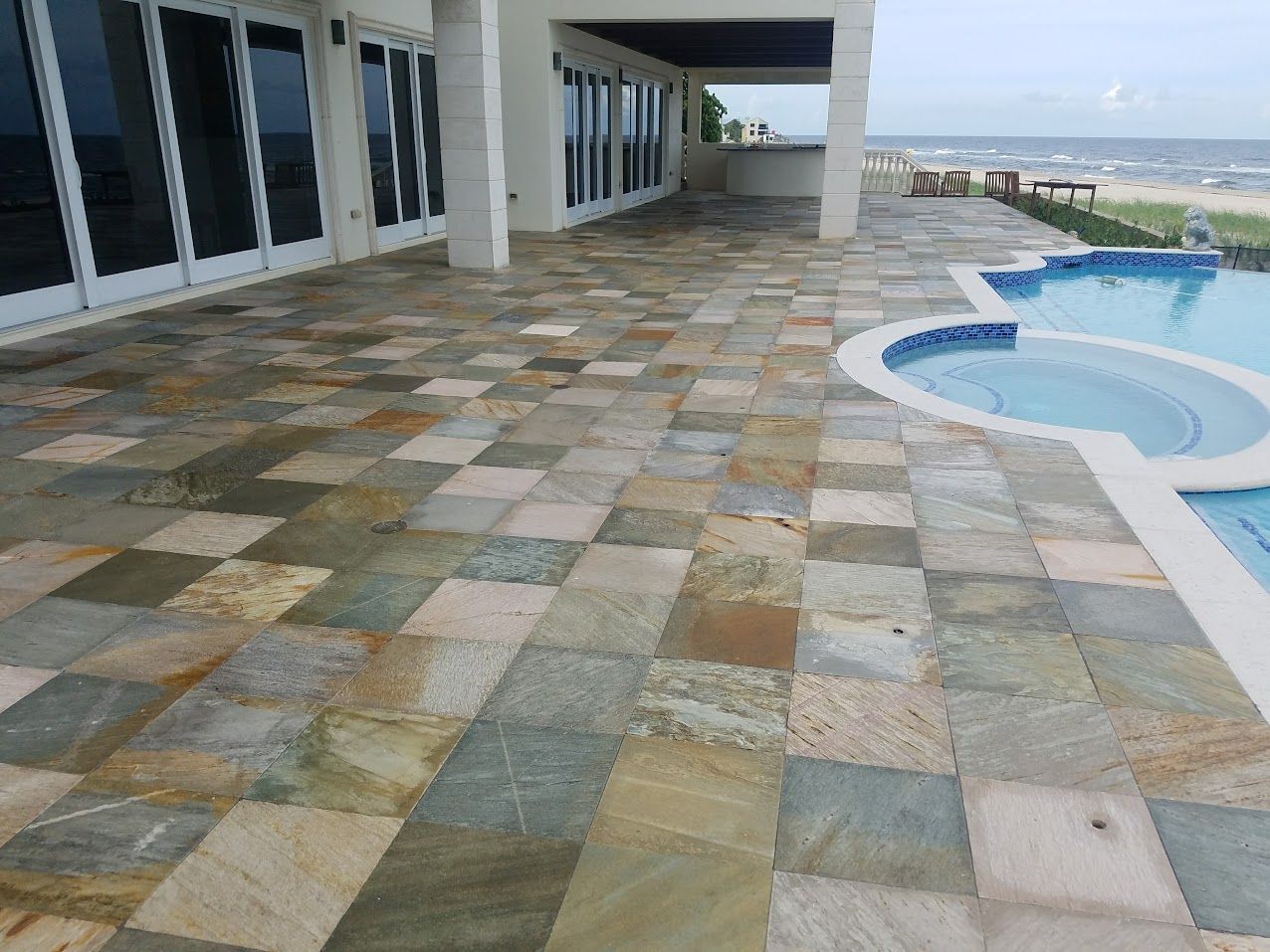 Stone-tiled poolside terrace with ocean view and a curved swimming pool