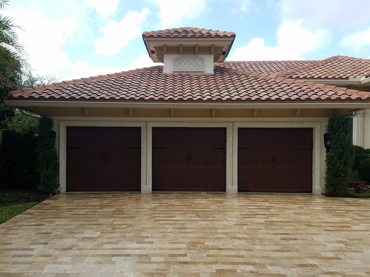Three-car garage with brown doors and a terracotta tile roof, viewed from a paved driveway.