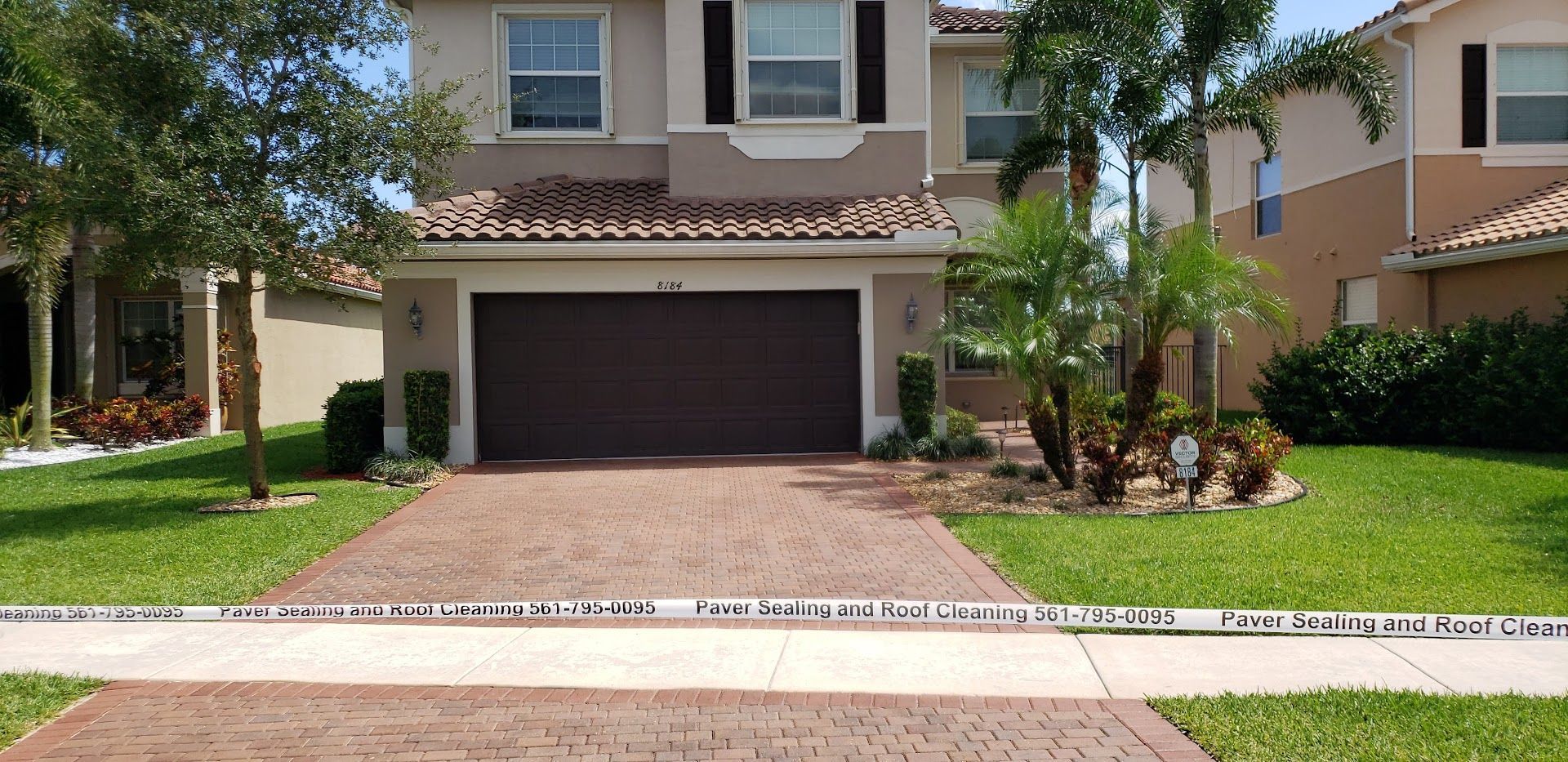 Suburban townhouse with a two-car garage, brick driveway, and palm trees in front