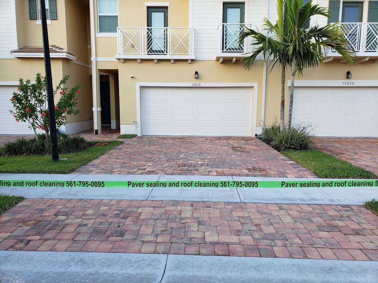 Suburban house exterior with beige stucco, white garage doors, and a brick driveway under palm trees
